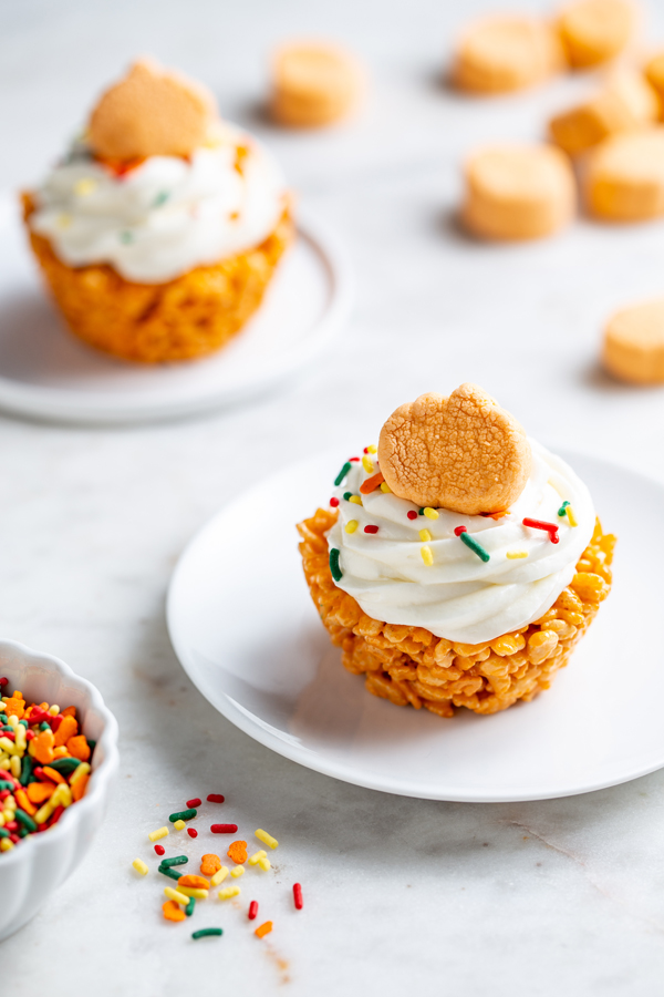 Pumpkin Spice Marshmallow Treat Cupcakes on counter with sprinkles and pumpkin marshmallows